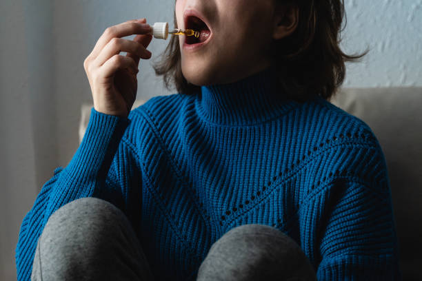 mujer joven tomando aceite de cbd debajo de la lengua - concepto de medicina alternativa - enfoque en el gotero - pipeta fotografías e imágenes de stock