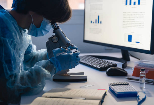 istock Female scientist worker in hazmat suit working with microscope and pc computer inside modern laboratory hospital - Medical research concept - Focus on microscope 1335692395