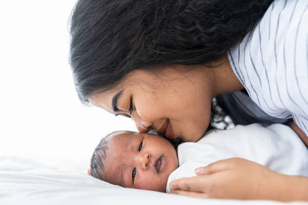 Mother kissing her newborn baby on the bed. Closeup of mom and infant baby Mother kissing her newborn baby on the bed. Closeup of mom and infant baby kissing photos stock pictures, royalty-free photos & images