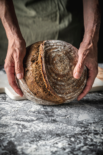 Male hands holding Sourdough bread brown round loaf wholegrain homemade German style on white flour background