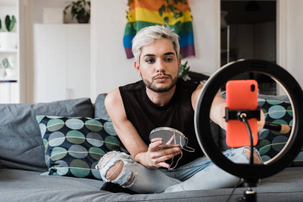 istock Gay man streaming online make up video tutorial with mobile phone indoors at home - Lgbt, drag queen, technology trendy concept - Focus in face 1335696463
