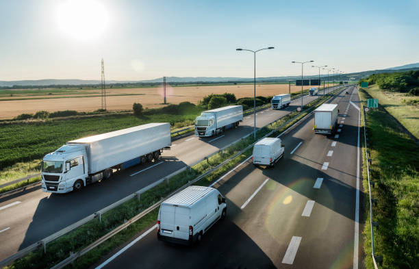 Highway Transit photo with Convoy of transportation trucks Convoy or caravans of transportation trucks passing vans and truck on a highway on a bright blue day. Highway transit transportation with lorry trucks and vans semi auto stock pictures, royalty-free photos & images