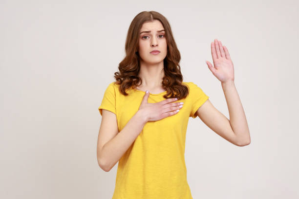 serious conscious brown haired woman of young age holding one hand on chest and raising another swearing, trust and honest, patriotism. - proof of love imagens e fotografias de stock