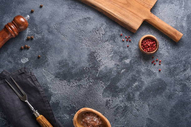 istock Old meat fork, black plate, black pepper and black pepper and spice mill on an old gray concrete background. Food cooking background and mock up. 1335710136