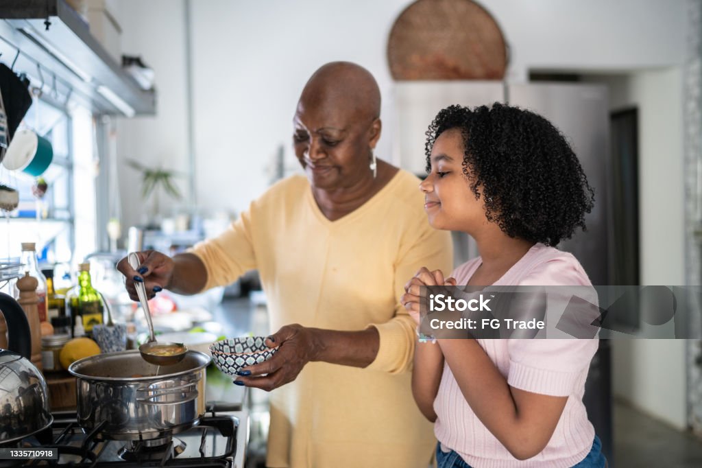 Grandmother serving soup bowl to granddaughter at home Soup Stock Photo