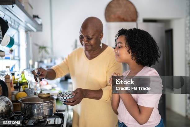 Grandmother Serving Soup Bowl To Granddaughter At Home Stock Photo - Download Image Now