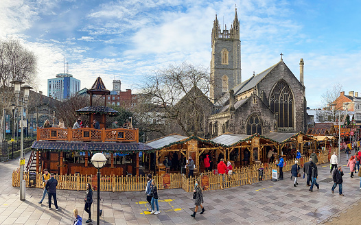 Cardiff, Wales - December 2020: People walking past stalls in the Cardiff Christmas Market. In the background is St John's church.