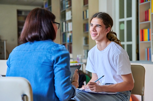 Maestra psicóloga escolar hablando y ayudando a estudiante, adolescente masculino photo