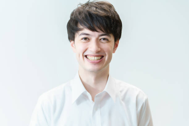 A young man wearing a white shirt and smiling in front of a white background