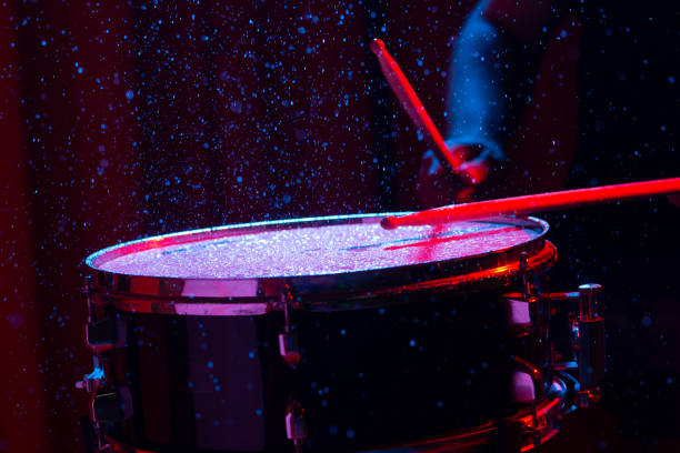 Drum sticks hitting snare drum with splashing water on dark background with red and blue  studio lighting. Dynamic scene. Drum sticks hitting snare drum with splashing water on dark background with red and blue  studio lighting. Dynamic scene. drummer hands stock pictures, royalty-free photos & images