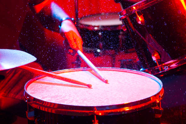 man playing the snare drum on a beautiful colored background, the concept of musical instruments with splashing water on dark background with red studio lighting. Dynamic scene. man playing the snare drum on a beautiful colored background, the concept of musical instruments with splashing water on dark background with red studio lighting. Dynamic scene. drum percussion instrument photos stock pictures, royalty-free photos & images