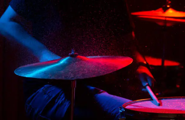 Photo of man plays musical percussion instrument with sticks with water splashes close up on a black background, play at the drum, red and blue lighting on the stage