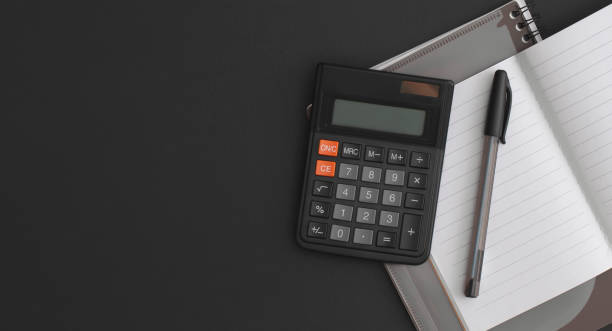 istock Calculator, notebook, pen on black leather background. Top view with copy space. Flat lay composition. 1335724749