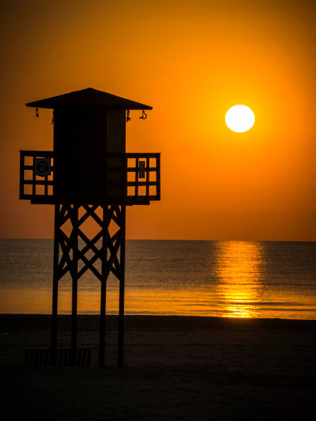 日の出時に太陽を背景にしたバレンシアのビーチでライフガードのための望楼 - lifeguard orange nature beach ストックフォトと画像