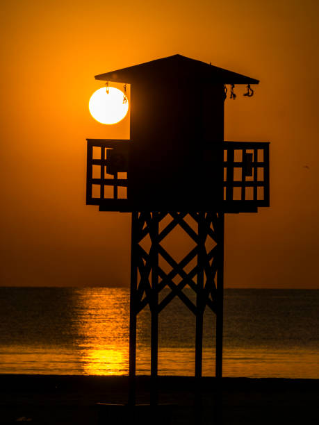 日の出時に太陽を背景にしたバレンシアのビーチでライフガードのための望楼 - lifeguard orange nature beach ストックフォトと画像