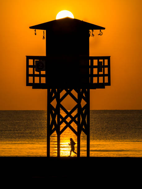 日の出時に太陽を��背景にしたバレンシアのビーチでライフガードのための望楼 - lifeguard orange nature beach ストックフォトと画像