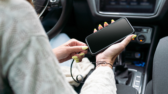 Female hands connects the charging cable to the phone in the car