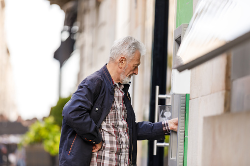 Elegant Elderly Man is Withdrawing Money from ATM in the Streets of the City District.