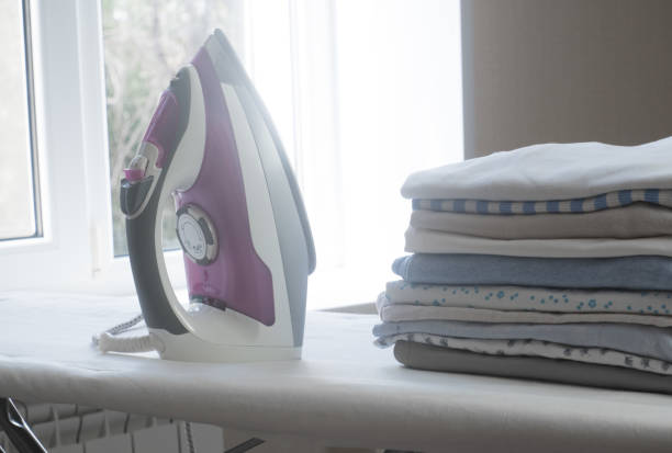 istock Stack of clean clothes and electric iron on board 1335774862