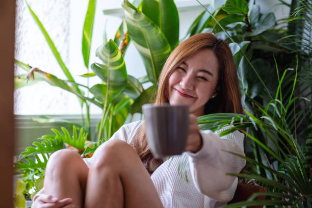 istock A beautiful asian woman holding and showing coffee cup while relaxing on balcony with houseplants garden at home 1335793729