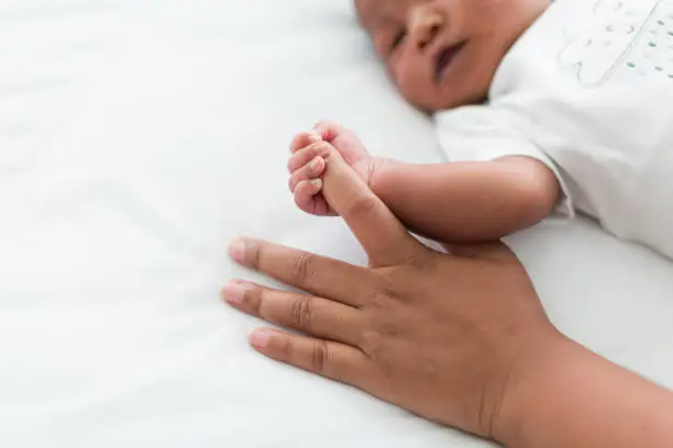 Photo of Newborn baby holding motherâs finder and sleeping in blanket on white bed