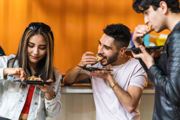 group of friends dining tacos at night in a street business three latinos eating tacos in taqueria taco stock pictures, royalty-free photos & images