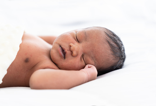 Newborn baby sleeping with blanket on white bed. Infant lying on white bed. African American newborn baby. Afro infant