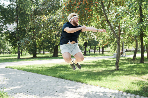 Overweight young man jumping during his sports training in the park in sunny day