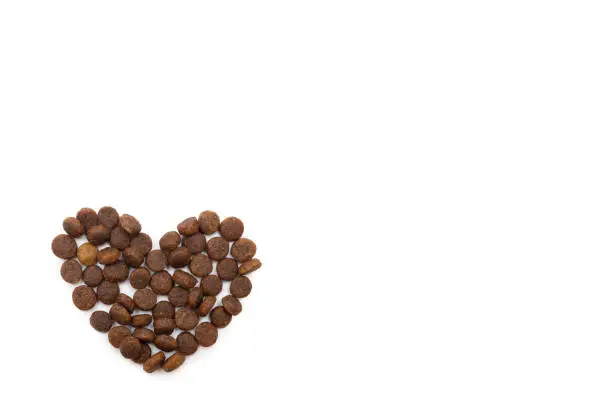 Photo of Dry pet food for dogs and cats in the shape of a heart isolated on white background, copy space, top view.