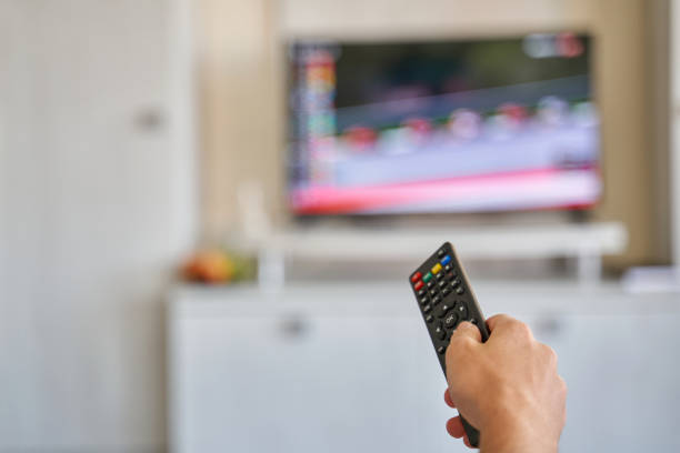 istock Young man holding remote control in hand while watching TV at home 1335827669
