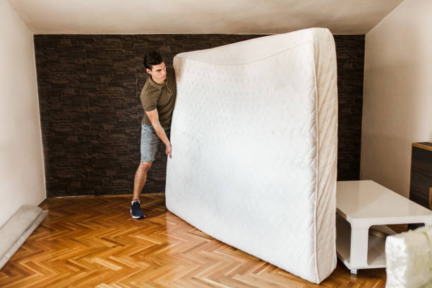 un hombre lleva un colchón mientras se muda fuera del apartamento - colchones fotografías e imágenes de stock