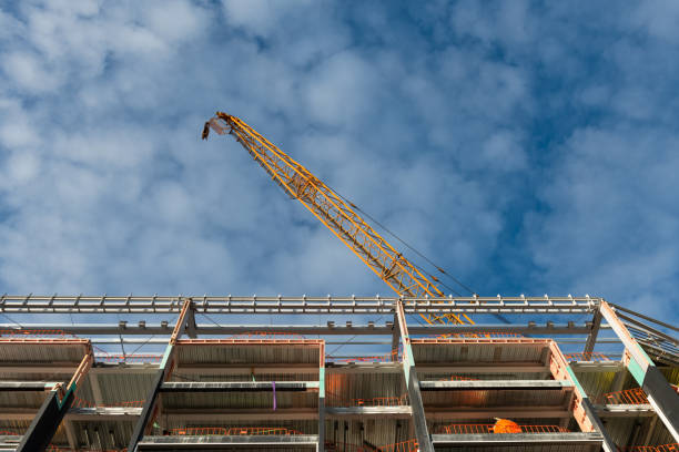 istock Apartment under construction with orange crane, low angle view. Blue sky with fluffy white clouds. 1335835246