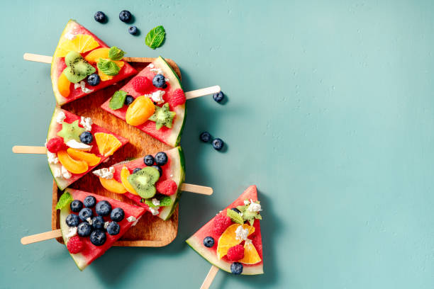 Watermelon pizza bar on blue table. Watermelon with assorti of berries, fruits and ricotta cheese. Pieces of watermelon with kiwi, blueberries, raspberries, apricots and orange on wooden board. Watermelon pizza bar on blue table. Watermelon with assorti of berries, fruits and ricotta cheese. Pieces of watermelon with kiwi, blueberries, raspberries, apricots and orange on wooden board. fruit salad stock pictures, royalty-free photos & images