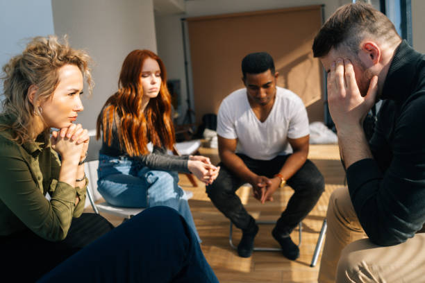 istock Close-up side view of sad depressed young man talking about problems on group interpersonal therapy session sitting on chairs in circle. 1335839577