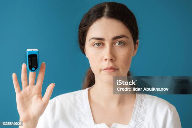 Portrait Of Woman Doctor Shows A Pulse Oximeter On Her Index Finger Blue Background The Concept Of Check Health And Medical Insurance Stock Photo - Download Image Now