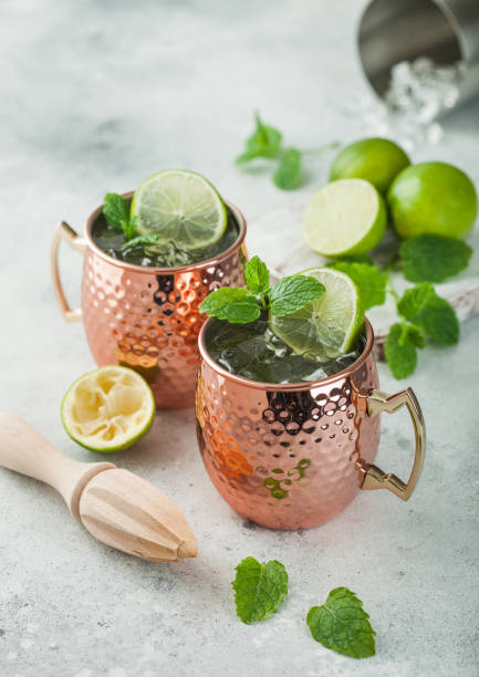 istock Moscow mule cocktail in a copper mug with lime and mint and wooden squeezer on light background with steel shaker 1335841563