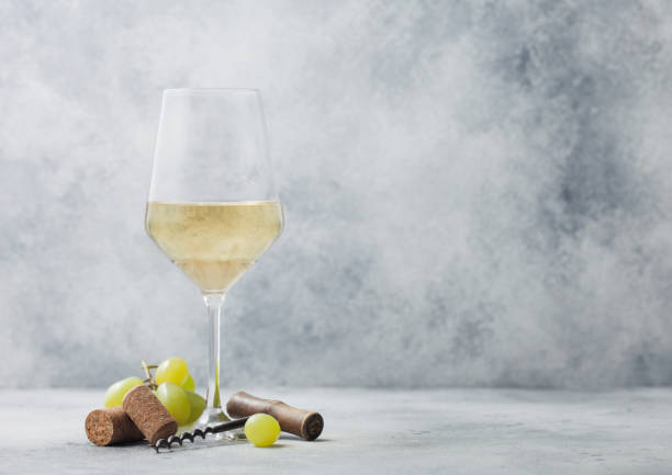 istock Glass of summer white wine with grapes, corks and corkscrew on light background. 1335842090