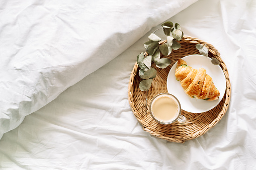 Breakfast in bed with croissant and coffee on tray.