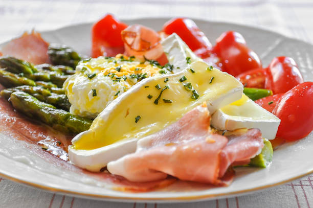 istock Delicious green boiled asparagus, ham, prosciutto, grape tomatoes, poached organic egg and brie cheese 1335844934