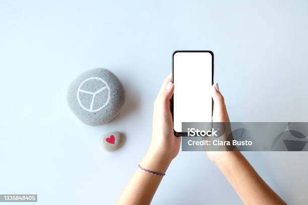 Young Female Hands Holding A Smartphone With Empty Screen Useful Template For Presentation Of Website Or App Symbols Of Peace And Love On The Side Stock Photo - Download Image Now