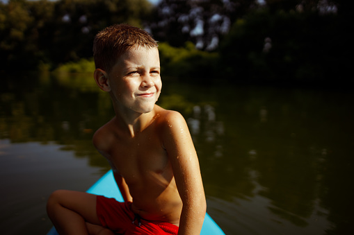 A joyful boy is playing with the SUP board and having fun in the emerald green water.