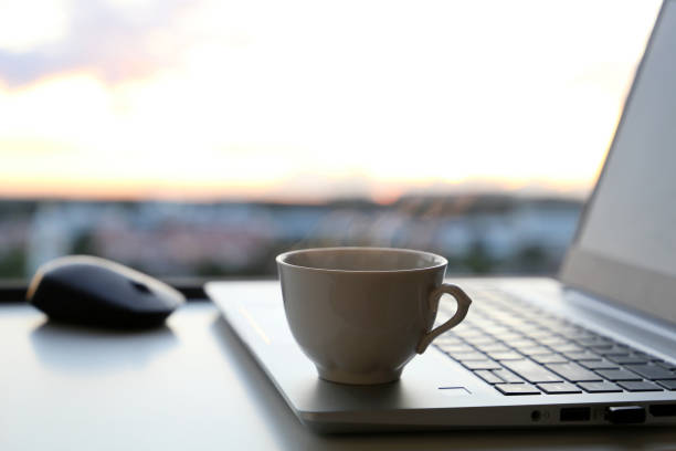 istock Hot coffee cup and laptop on table against the window at sunrise 1335852033