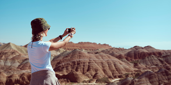 asian woman tourist taking a picture of the yardang landforms using mobile phone in national geological park, rear view