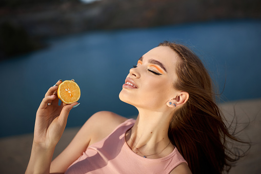 Woman with a lemon in her hands, beauty skin nutrition with vitamin C. Natural cosmetics for facial skin care. Sunny day blue sky