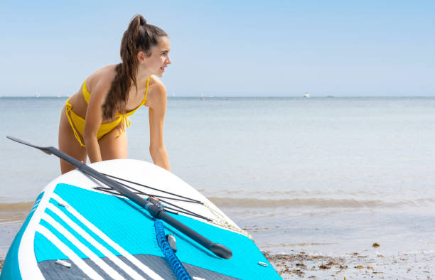 jeune femme de race blanche traînant une planche de surf à pagaie de la plage à la mer - fitness trainer photos et images de collection
