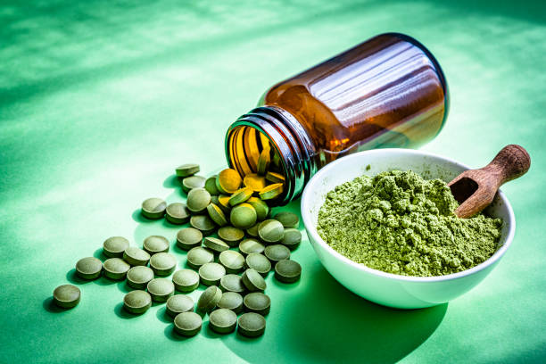 Nutritional supplement: Moringa powder in a white bowl and Moringa capsules spilling out a bottle shot on green background. High resolution 42Mp studio digital capture taken with Sony A7rII and Sony FE 90mm f2.8 macro G OSS lens