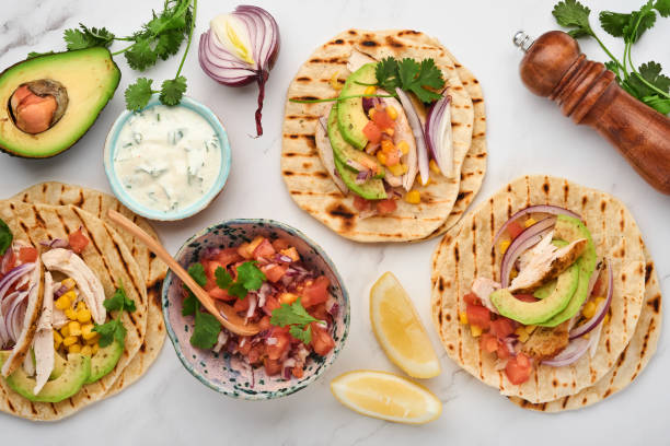 istock Mexican tacos with grilled chicken, avocado, corn kernels, tomato, onion, cilantro and salsa at white stone table. Traditional Mexican and Latin american street food. Top view. 1335855510