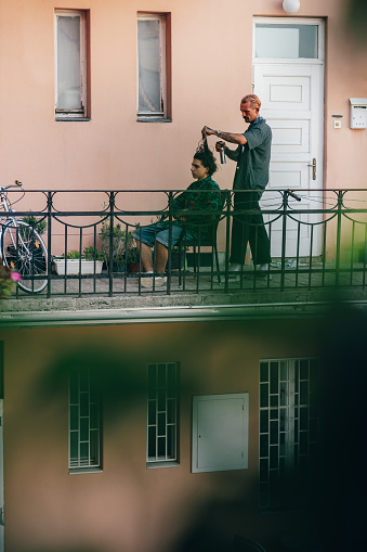 Male hairdresser styling and treating a man's hair on balcony
