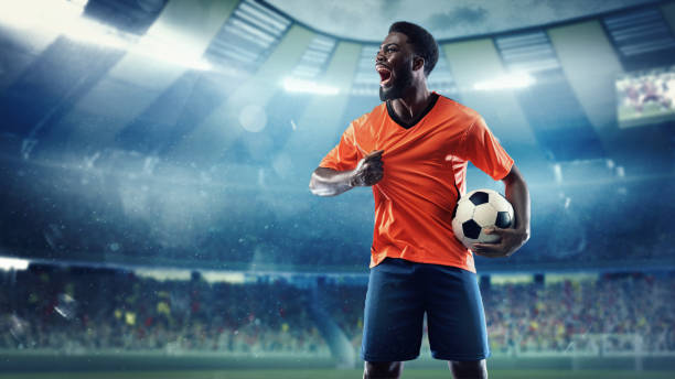 African -american football or soccer player at stadium in flashlights - motion, action, activity, competition concept Winner, champion. Football or soccer player at stadium in flashlight. Young male sportsman after goal in playing time. Looks excited, overjoyed. Concept of sport, competition, winning, action. stadium advertising stock pictures, royalty-free photos & images