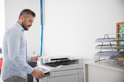 Office clerk pushing buttons for programming photocopier in the office, copying documents